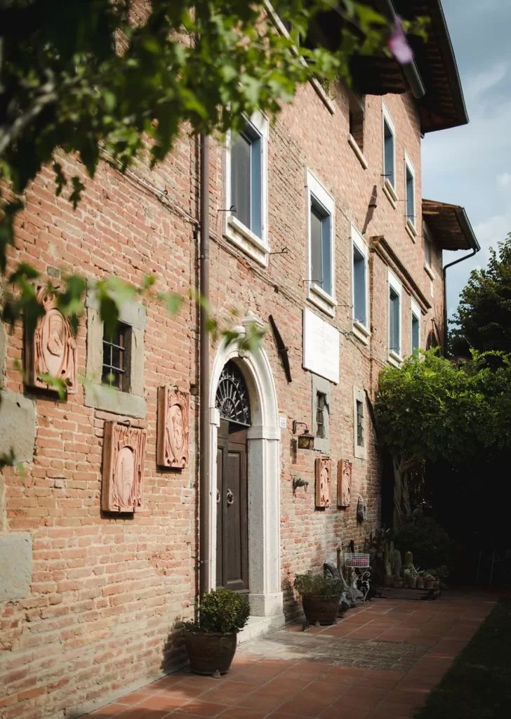 Rustic brick façade of Borgo Tre Rose adorned with terracotta art and lush greenery.