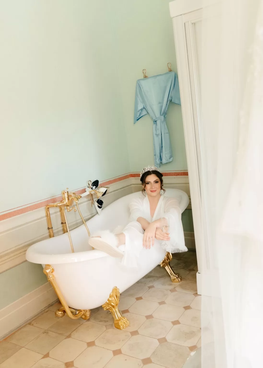 Bride relaxing in a clawfoot bathtub at Villa Ivana Cortona, wearing a tiara and sipping champagne in her bridal robe.