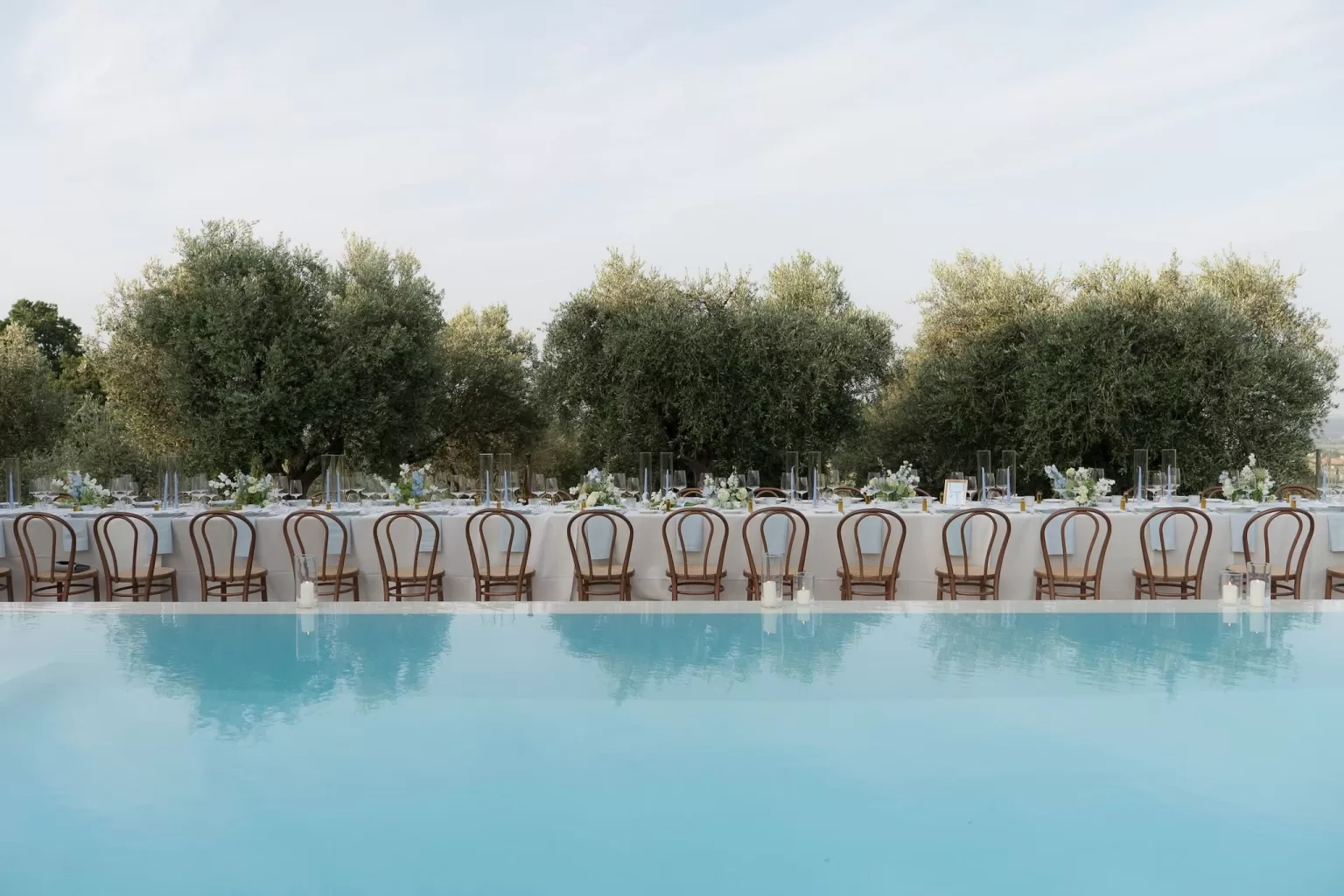 Long wedding table beside the pool at Casa Olivi, surrounded by olive trees and floral centrepieces.