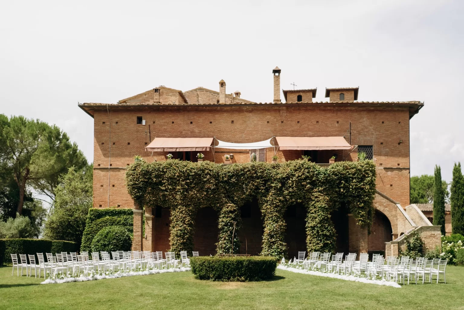 Wide view of outdoor ceremony setup with chairs facing ivy-covered villa at Castello di San Fabiano