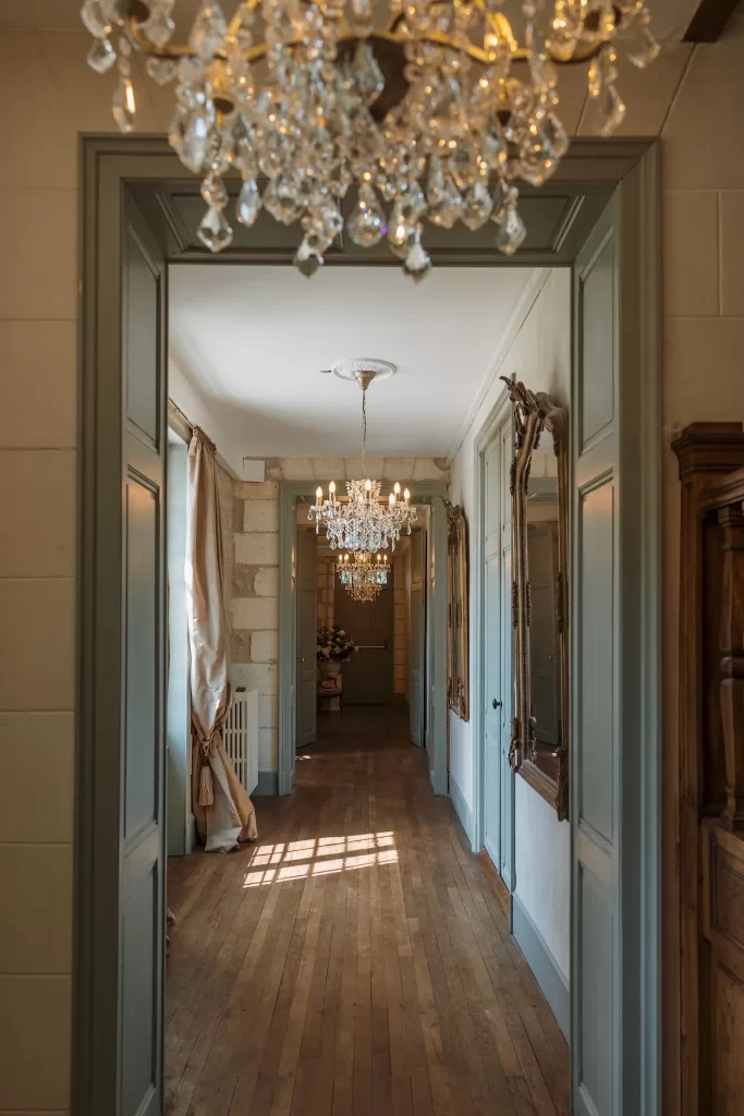Elegant hallway at Château de la Couronne with chandeliers, large mirrors, and wooden floors.