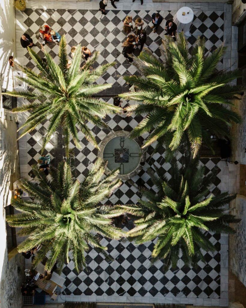 A wide-angle view of the checkered courtyard at Chateau de Garde, featuring its signature black-and-white pattern surrounded by lush greenery.