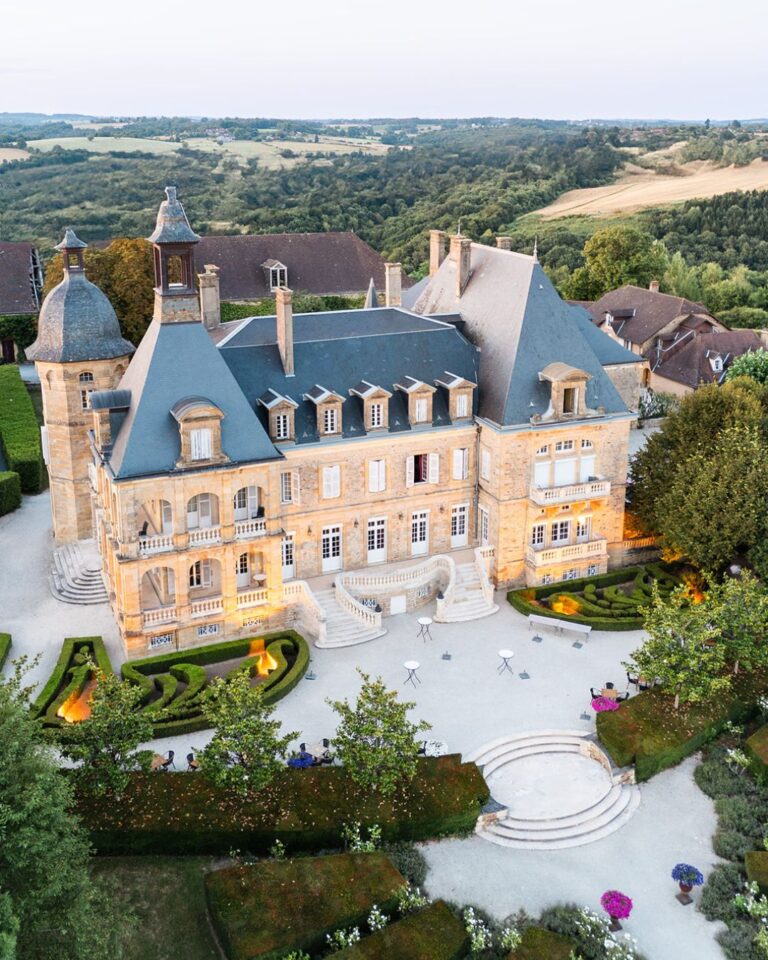 Stunning aerial view of Domaine d'Essendiéras château at dusk, highlighting its elegant gardens and warmly lit façade.
