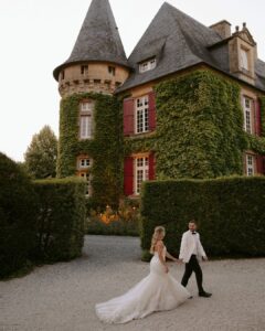 Hand in hand, the newlyweds stand before the château’s ivy-covered tower, capturing the timeless charm of the venue.
