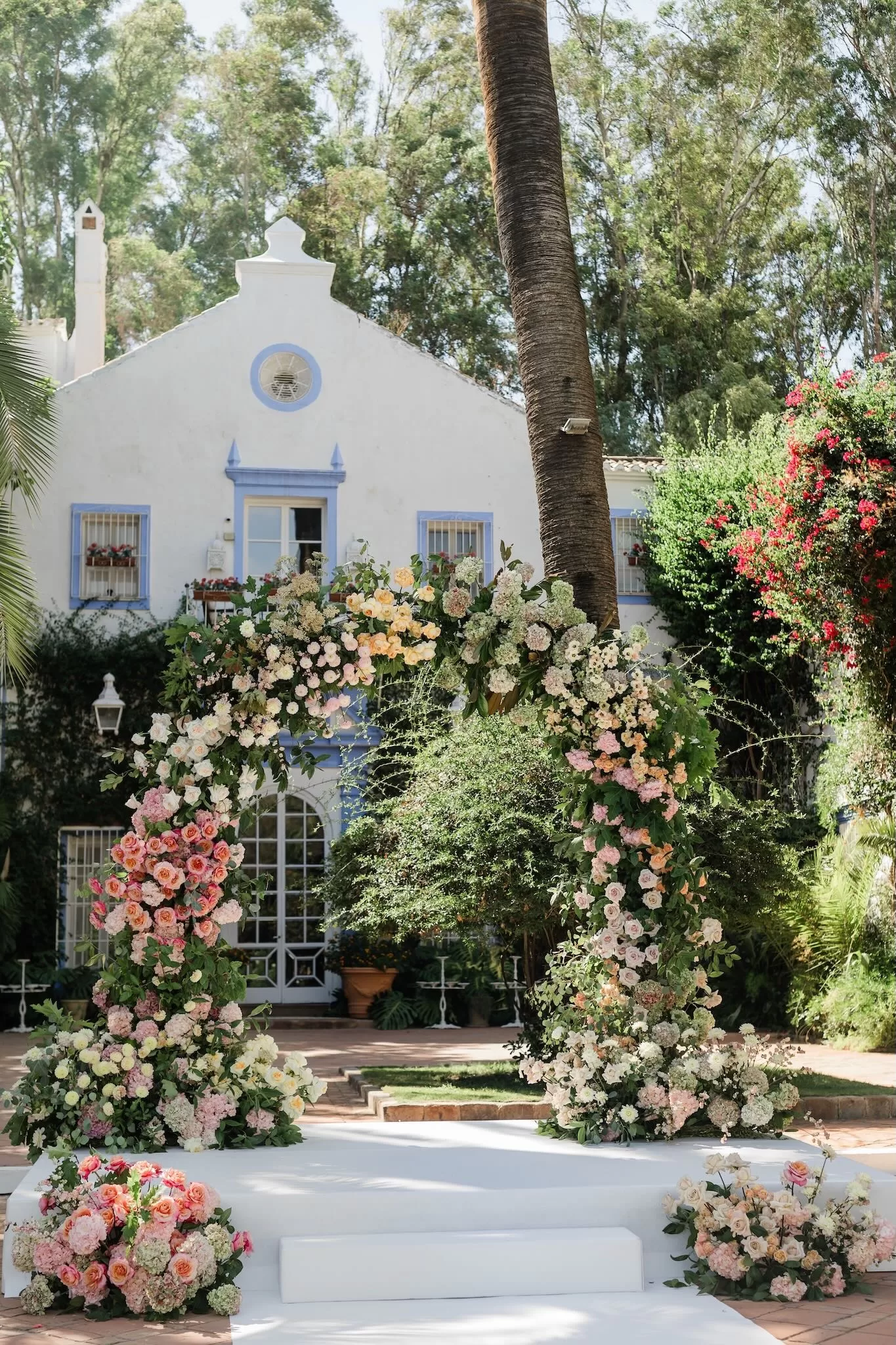 Lush pastel floral arch in front of the white villa facade at Finca la Concepción, ready for the wedding ceremony.