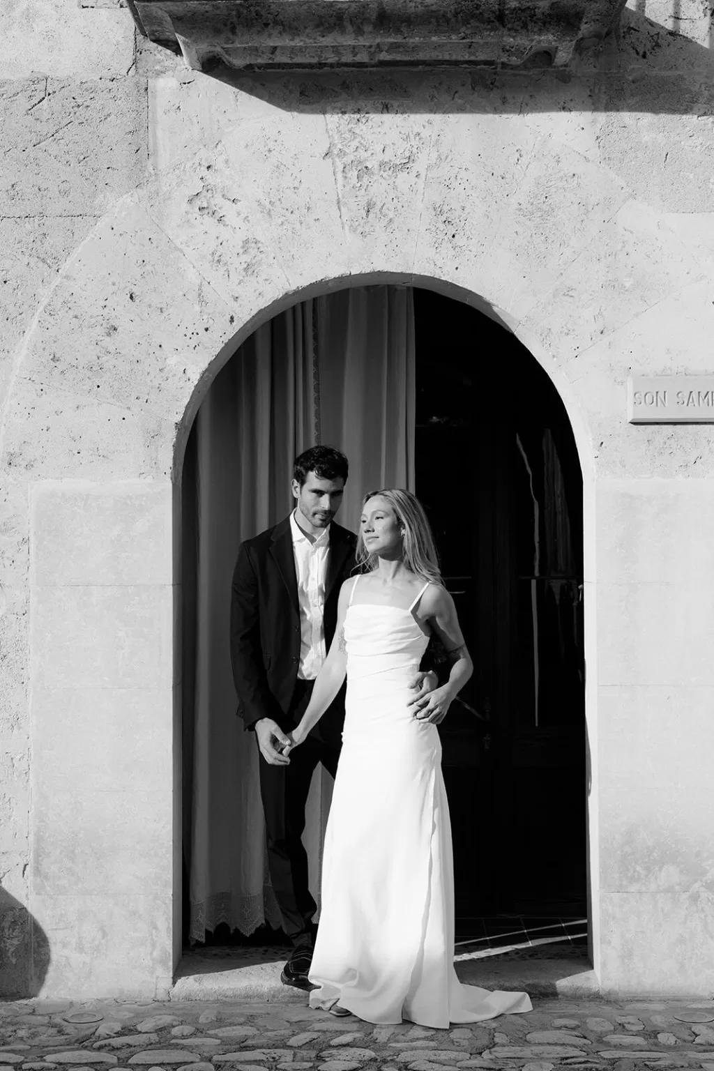 Bride and groom framed by the historic stone archway of Finca Son Sampol, bathed in soft afternoon light.