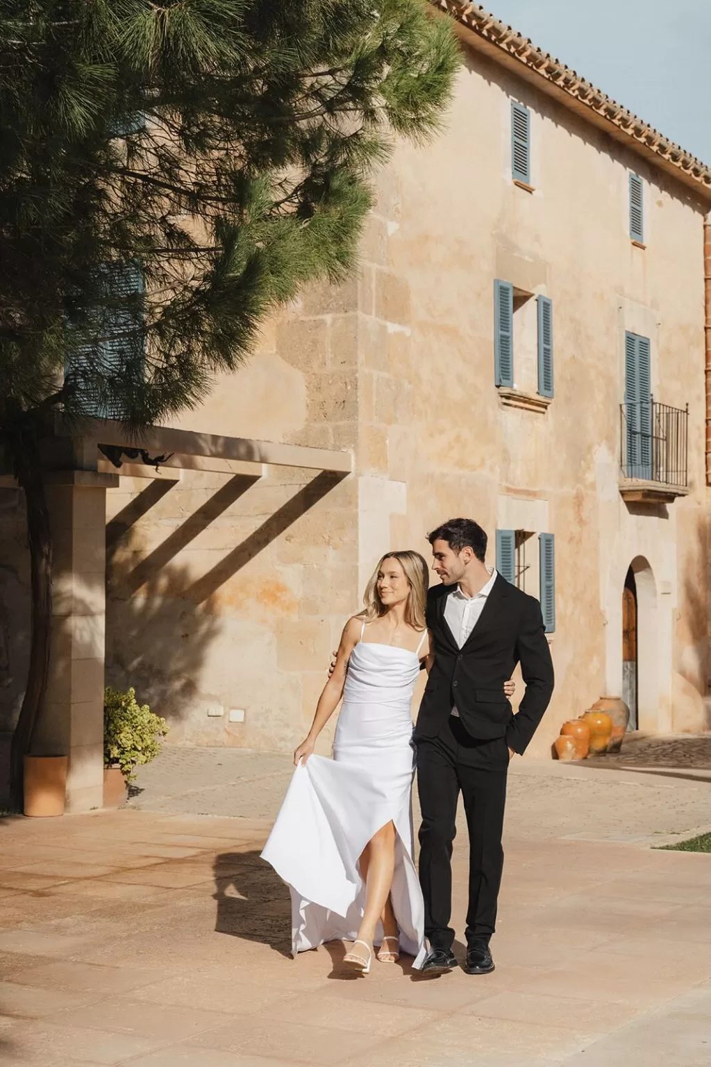 Bride and groom walking arm in arm by the rustic façade of Finca Son Sampol.