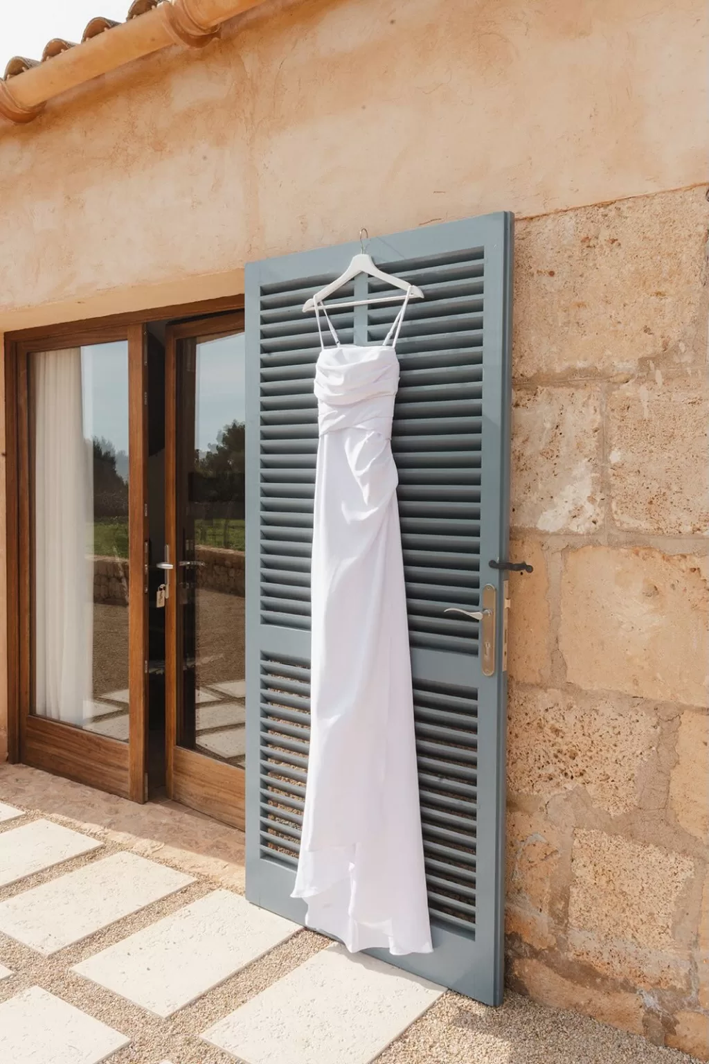 Minimalist white wedding dress hanging on blue shutter at Finca Son Sampol.