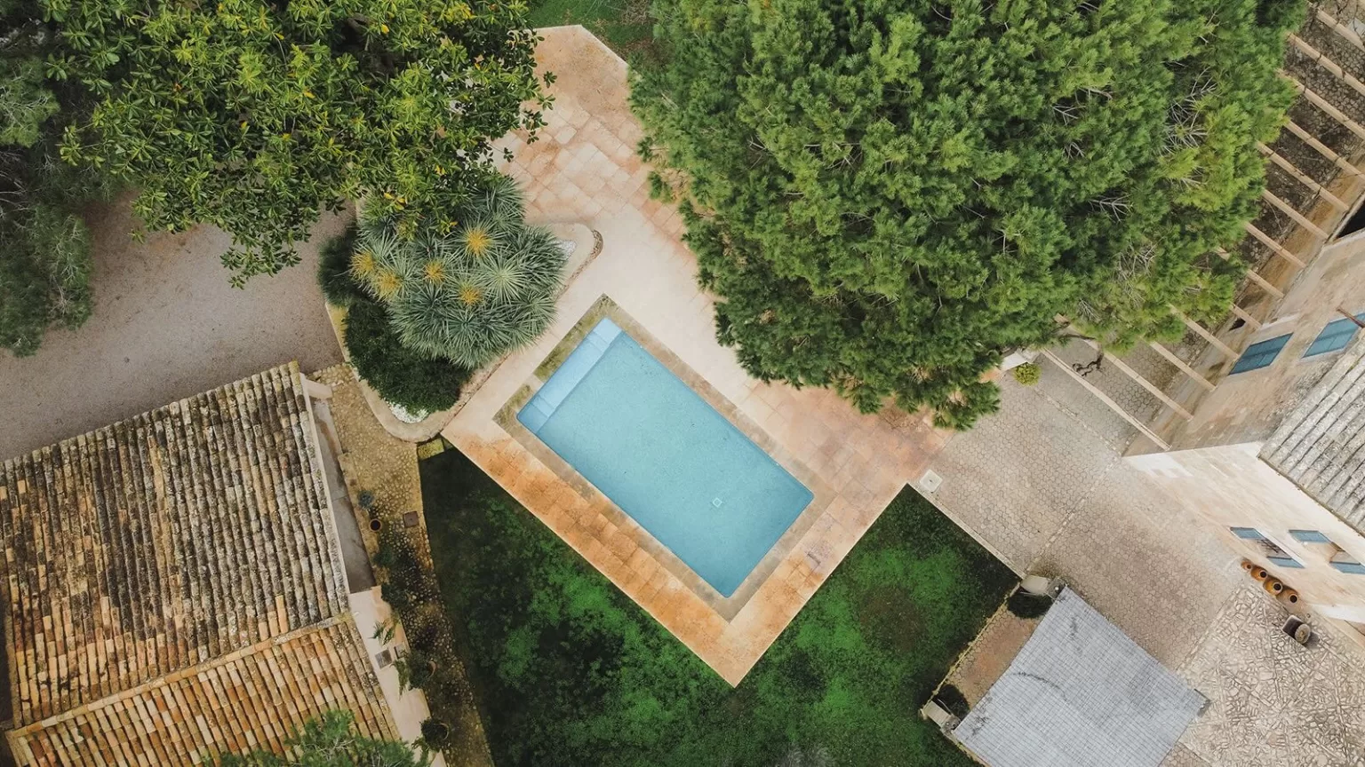 Aerial view of Finca Son Sampol showing the pool, rustic rooftops, and lush Mediterranean greenery surrounding the venue.