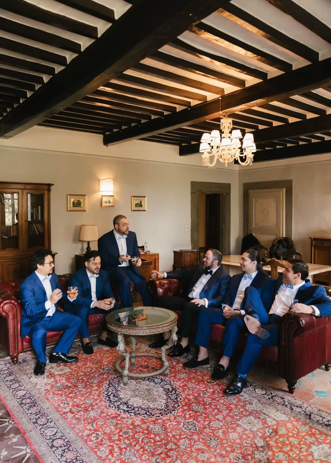 Groom and groomsmen enjoying drinks and laughter in the richly decorated sitting room of Villa Ivana Cortona.