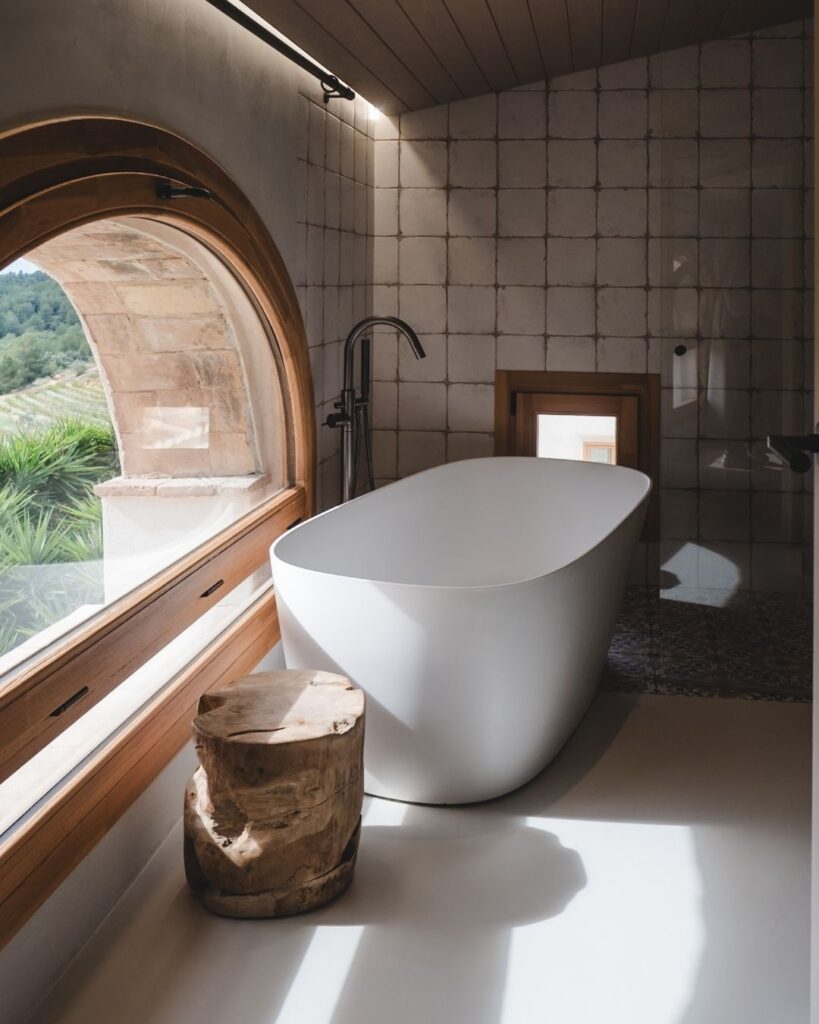 Beautiful freestanding bathtub placed next to a large arched window overlooking vineyards, capturing the serene setting at Masia Cabellut.