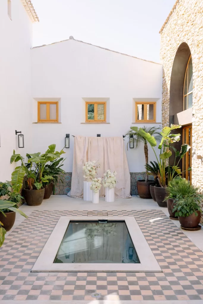 Intimate courtyard ceremony setup with white floral arrangements and tropical plants at Masia Cabellut.