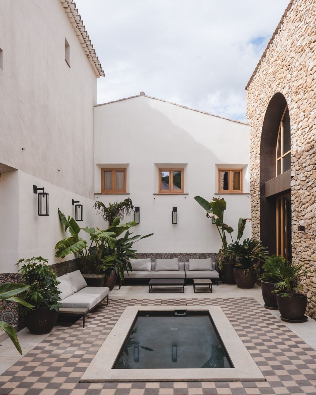 Stylish courtyard at Masia Cabellut featuring modern seating areas, vibrant greenery, and a tranquil pool.