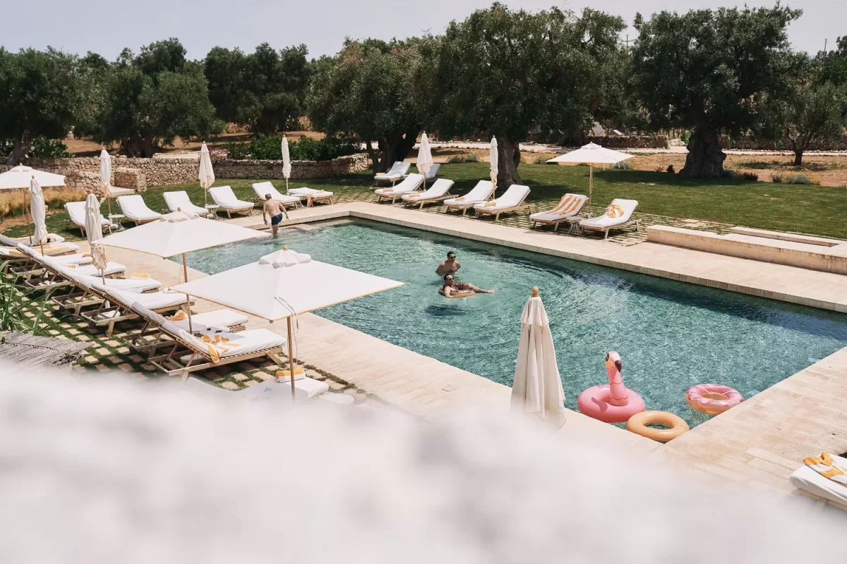 Guests enjoying a sunny swim in the pool surrounded by olive trees at Masseria Calderisi