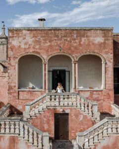 Stunning bride gazing out of a window at Masseria Spina, bathed in natural light and framed by rustic interiors, captured by Amali Studios.