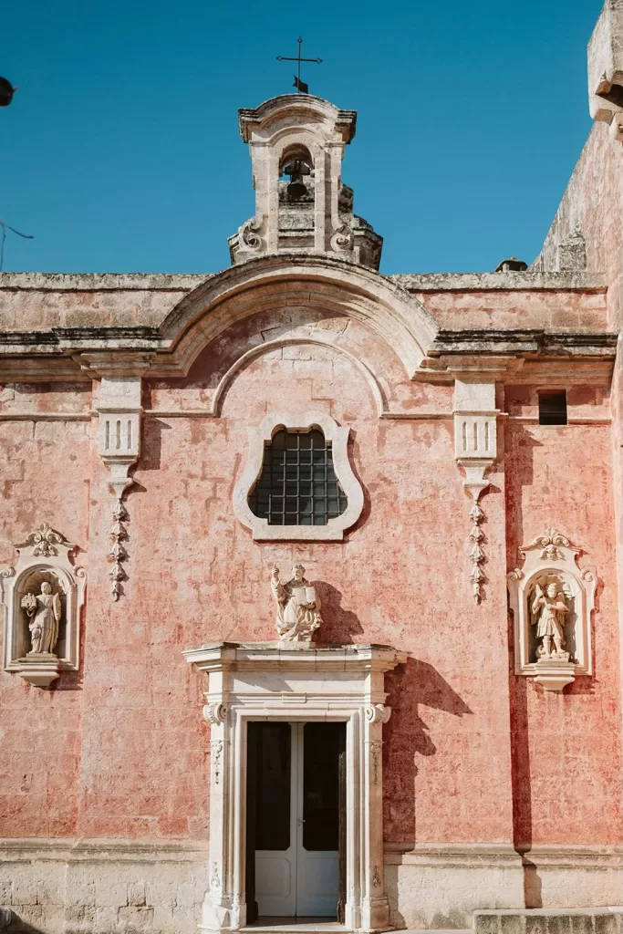 Architectural detail of Masseria Spina’s chapel with sculpted figures and pink stone walls.