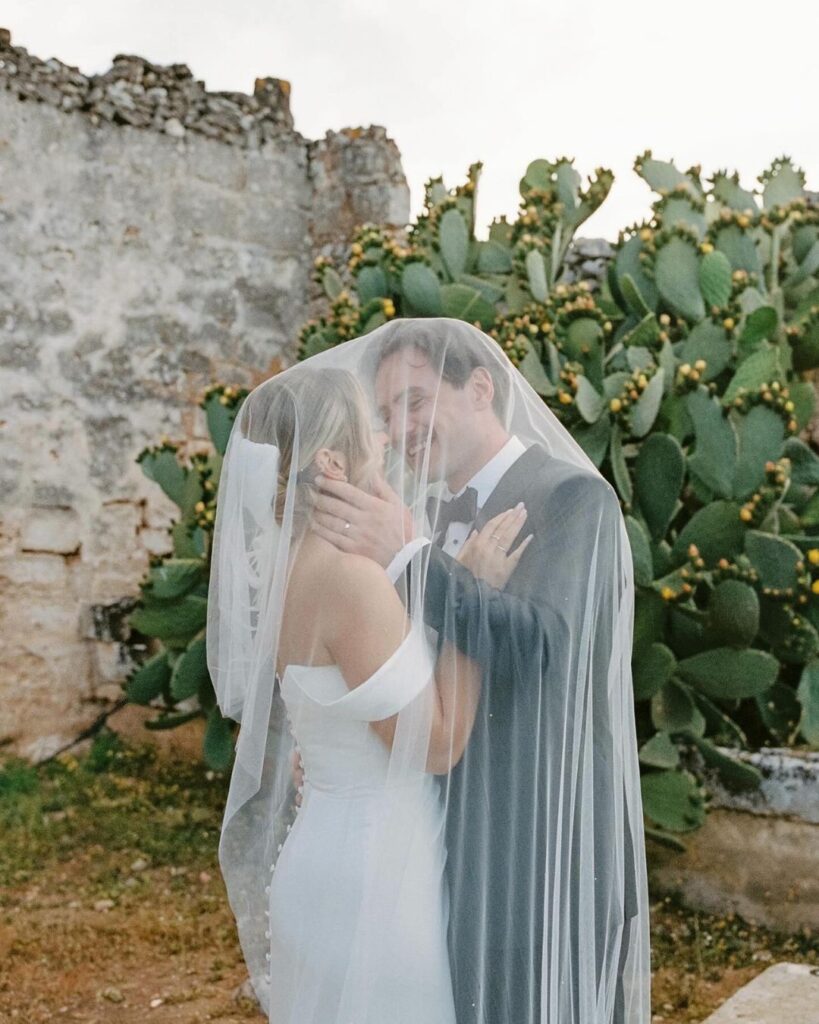 Bride and groom sharing a tender moment in the courtyard of Masseria Spina, surrounded by lush greenery, captured by Amali Studios.