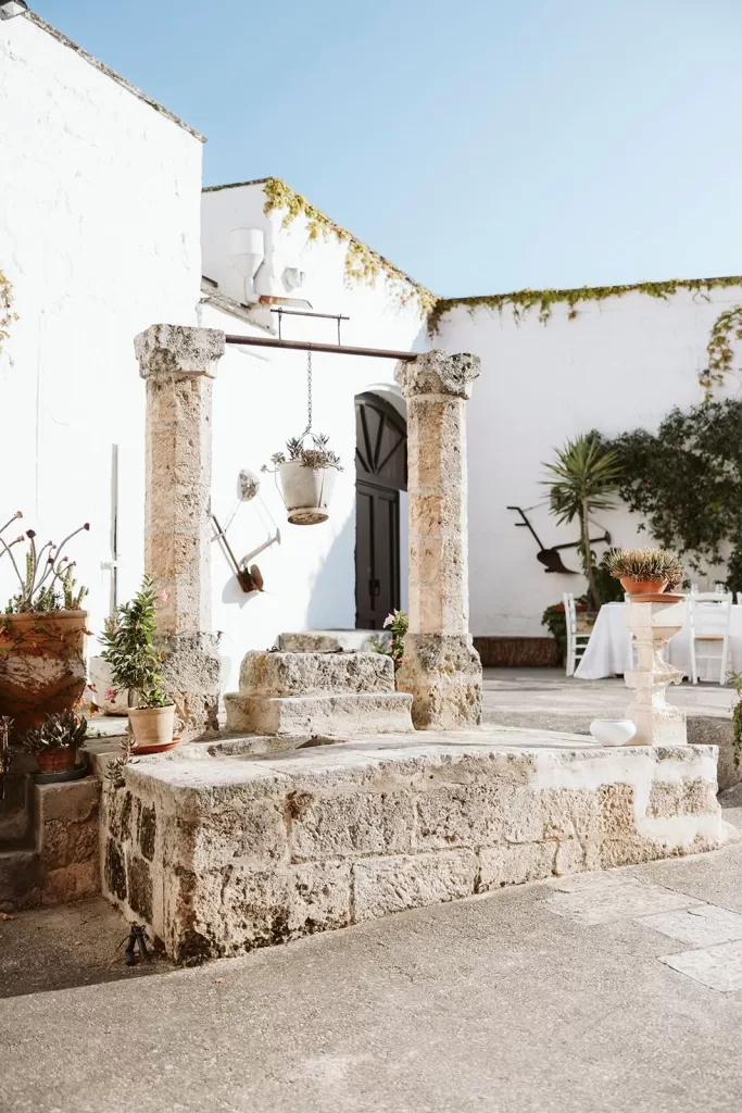Historic stone well in a sunlit courtyard surrounded by potted plants at Masseria Spina.