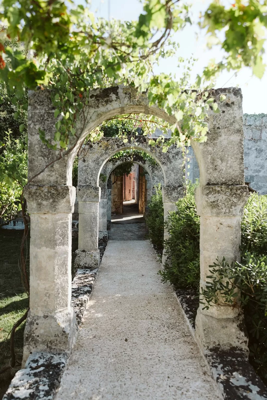 Stone archway pathway surrounded by lush greenery at Masseria Spina