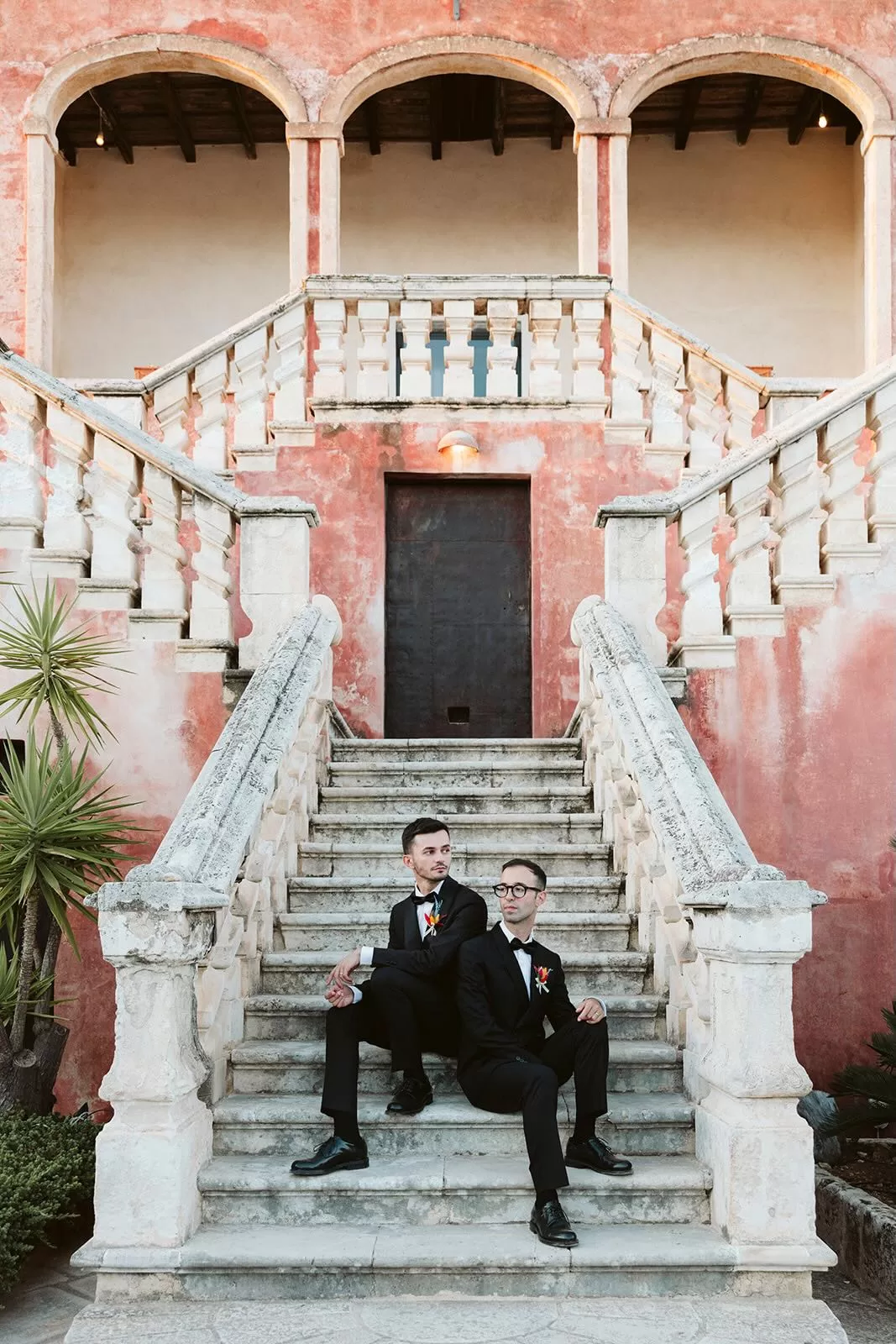 Grooms sitting on the stone staircase framed by arches at Masseria Spina.