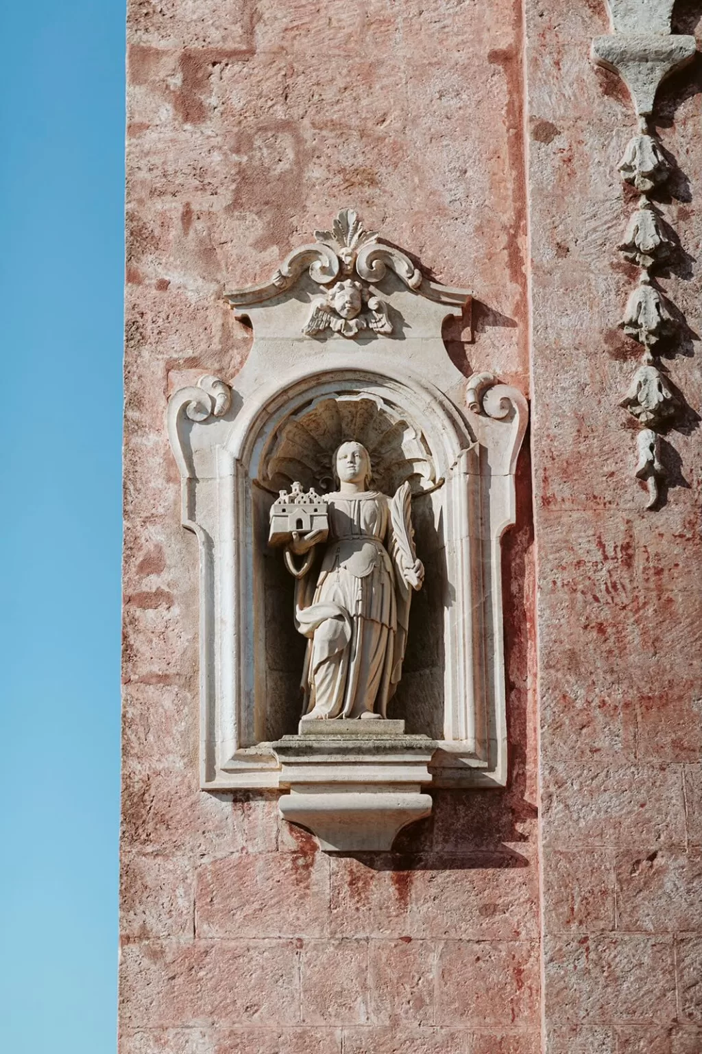 Architectural detail of a saint statue embedded in the weathered red walls of Masseria Spina, adding character to the venue’s façade.