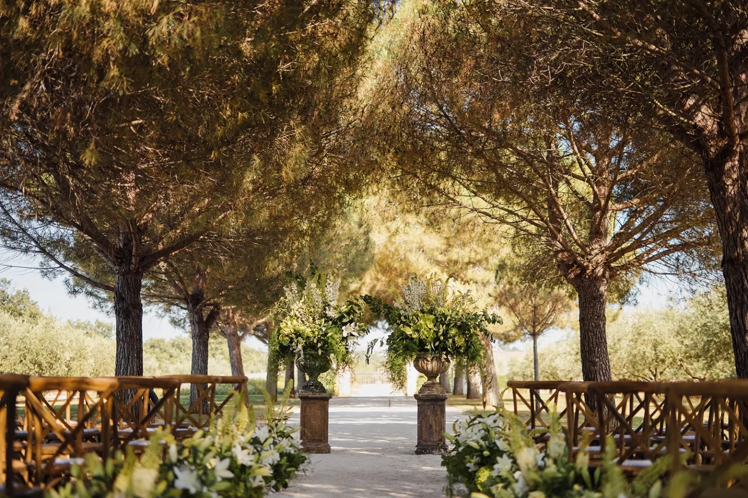 Elegant ceremony aisle under pine trees with grand floral urns at Meneghetti Wine Hotel.