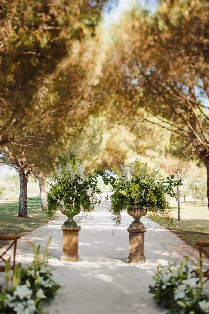 Oversized urns with green and white flowers marking the ceremony altar under pine trees at Meneghetti Wine Hotel.