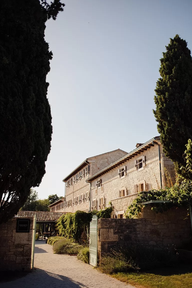Stone entrance to Meneghetti Wine Hotel with green iron gate, ivy-covered walls, and Mediterranean charm.