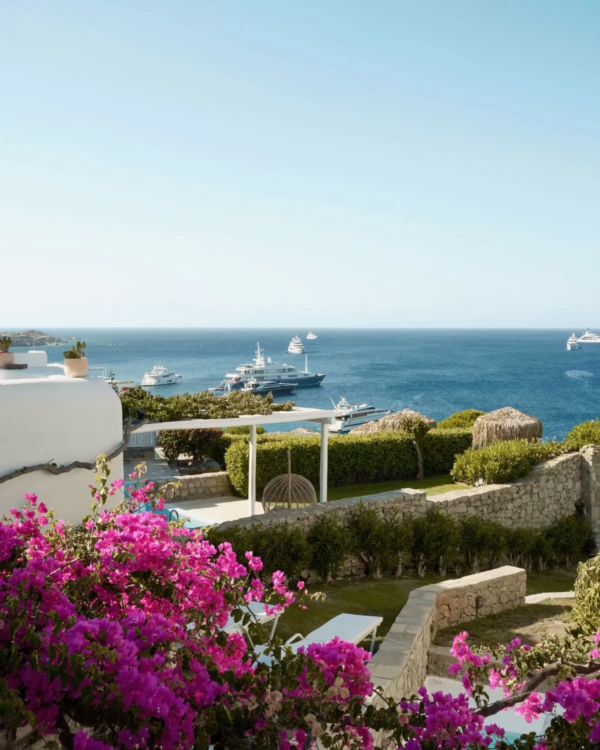 Bright pink bougainvillea framing a sea view with yachts anchored offshore at Mykonos Blu.