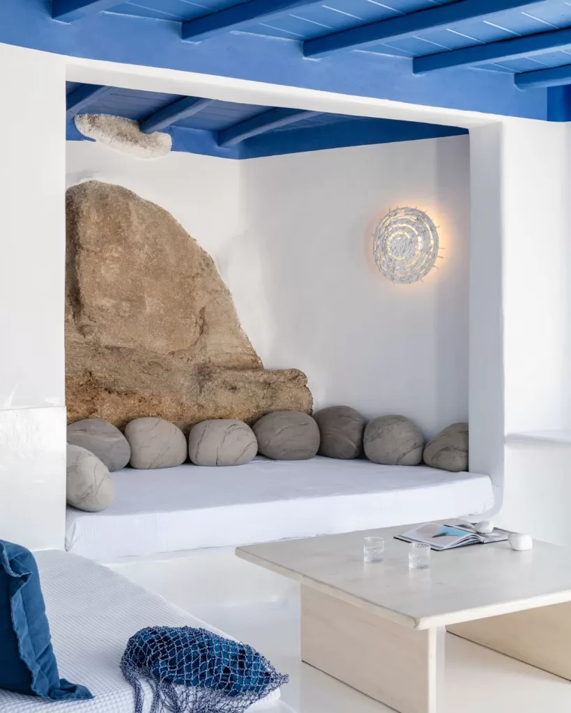 Coastal-inspired lounge at Mykonos Blu with natural rock feature, white walls, and blue ceiling.