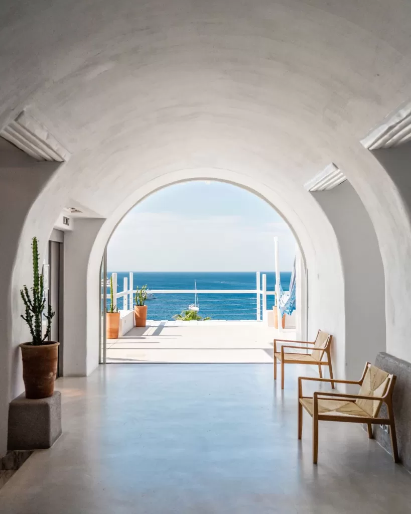 Framed sea view through a curved white archway at Mykonos Blu, leading to a sunlit terrace.