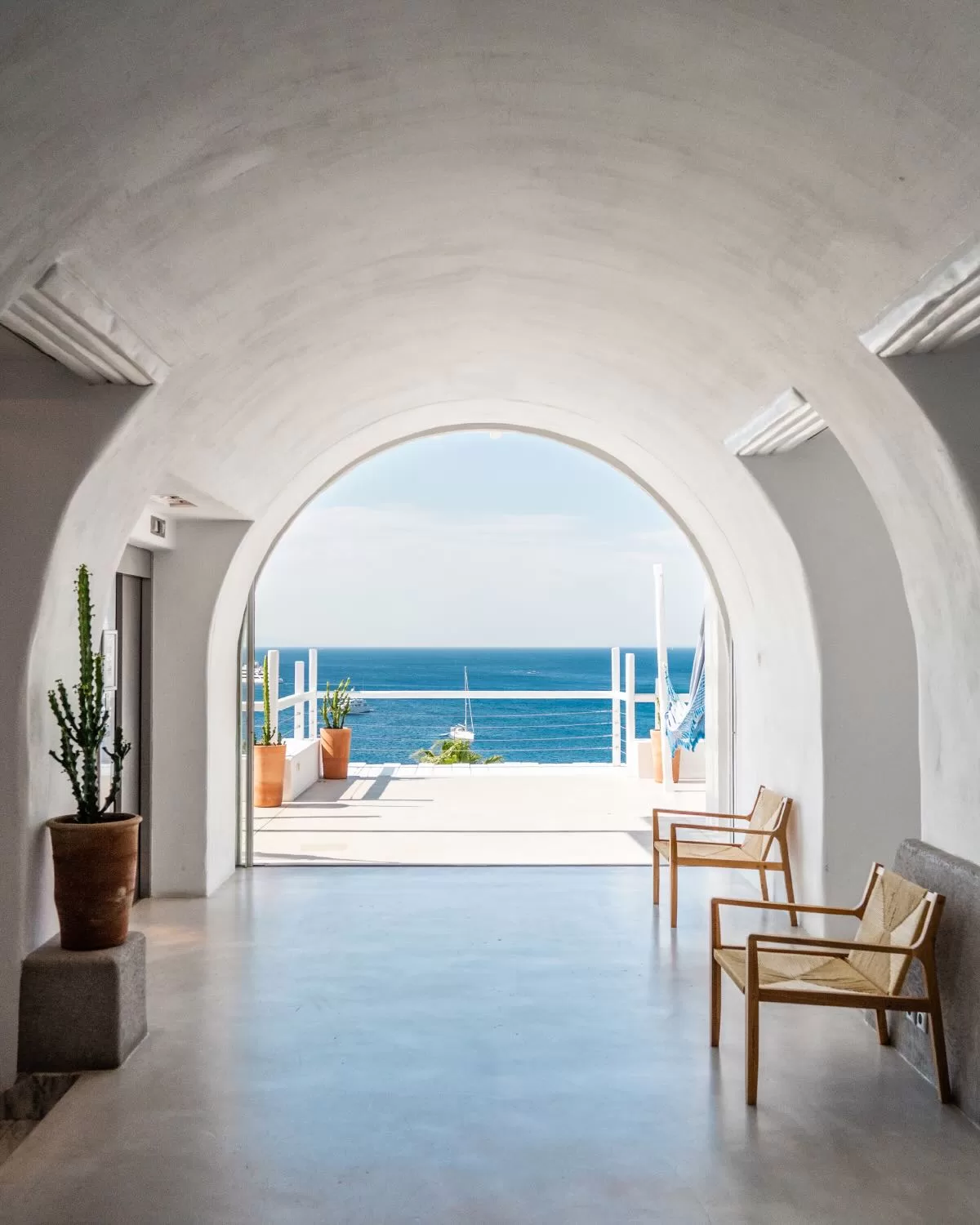 Framed sea view through a curved white archway at Mykonos Blu, leading to a sunlit terrace.