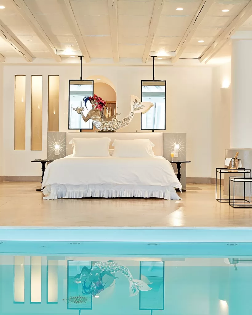 Elegant suite at Mykonos Blu with indoor pool and playful mermaid sculpture, reflecting in the water.