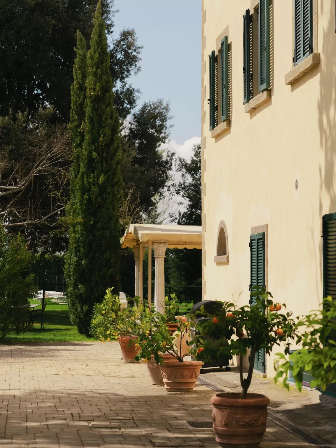 Terracotta pots with citrus trees and classic green shutters on the sunlit patio of Villa Ivana Cortona.