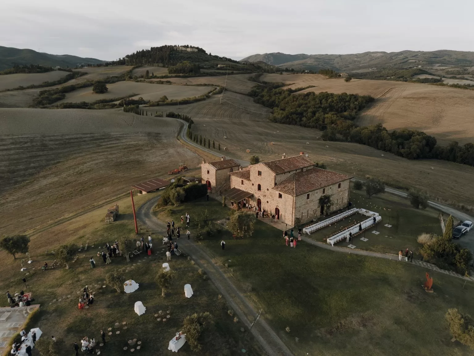 Aerial view of Podere Calvaiola showing the rustic villa, long reception tables, and guests gathering on the lawn.