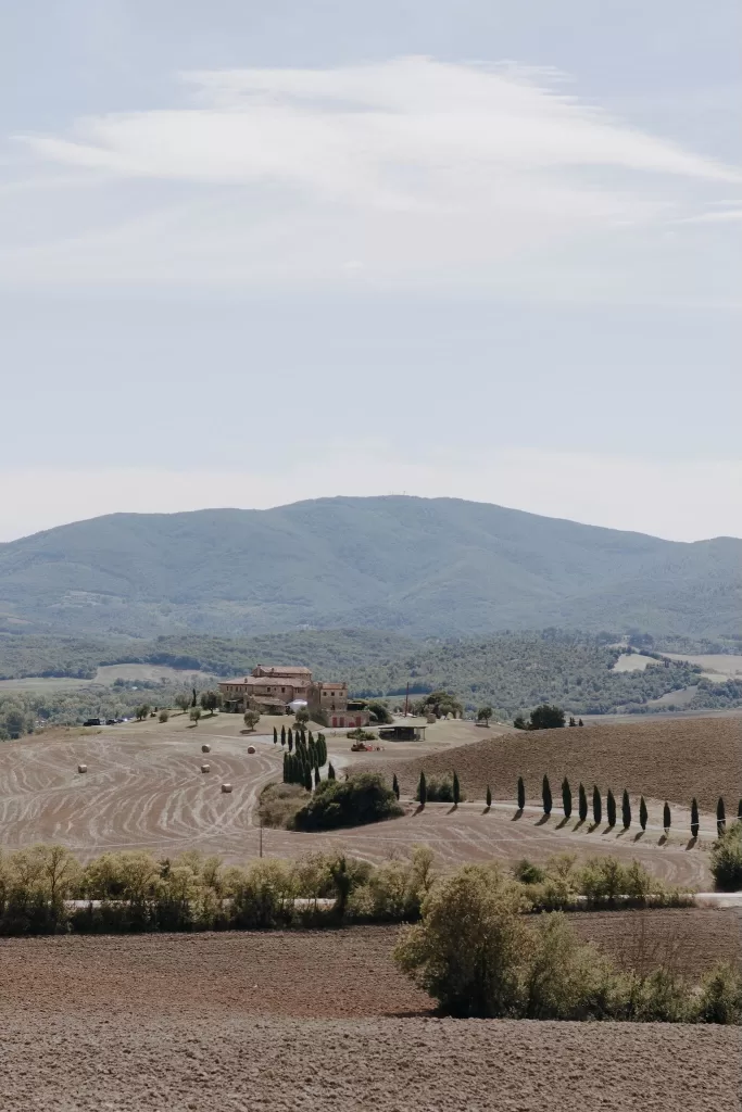 Elevated view of Podere Calvaiola villa nestled in golden fields with mountain backdrop