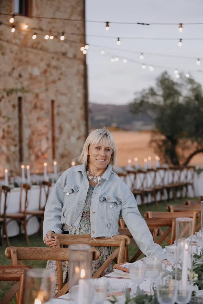 Wedding planner adjusts chairs under string lights at Podere Calvaiola, preparing for the evening reception