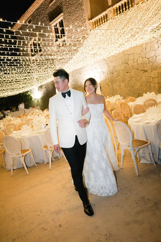 Bride and groom walking through reception space under warm string lights at Son Marroig