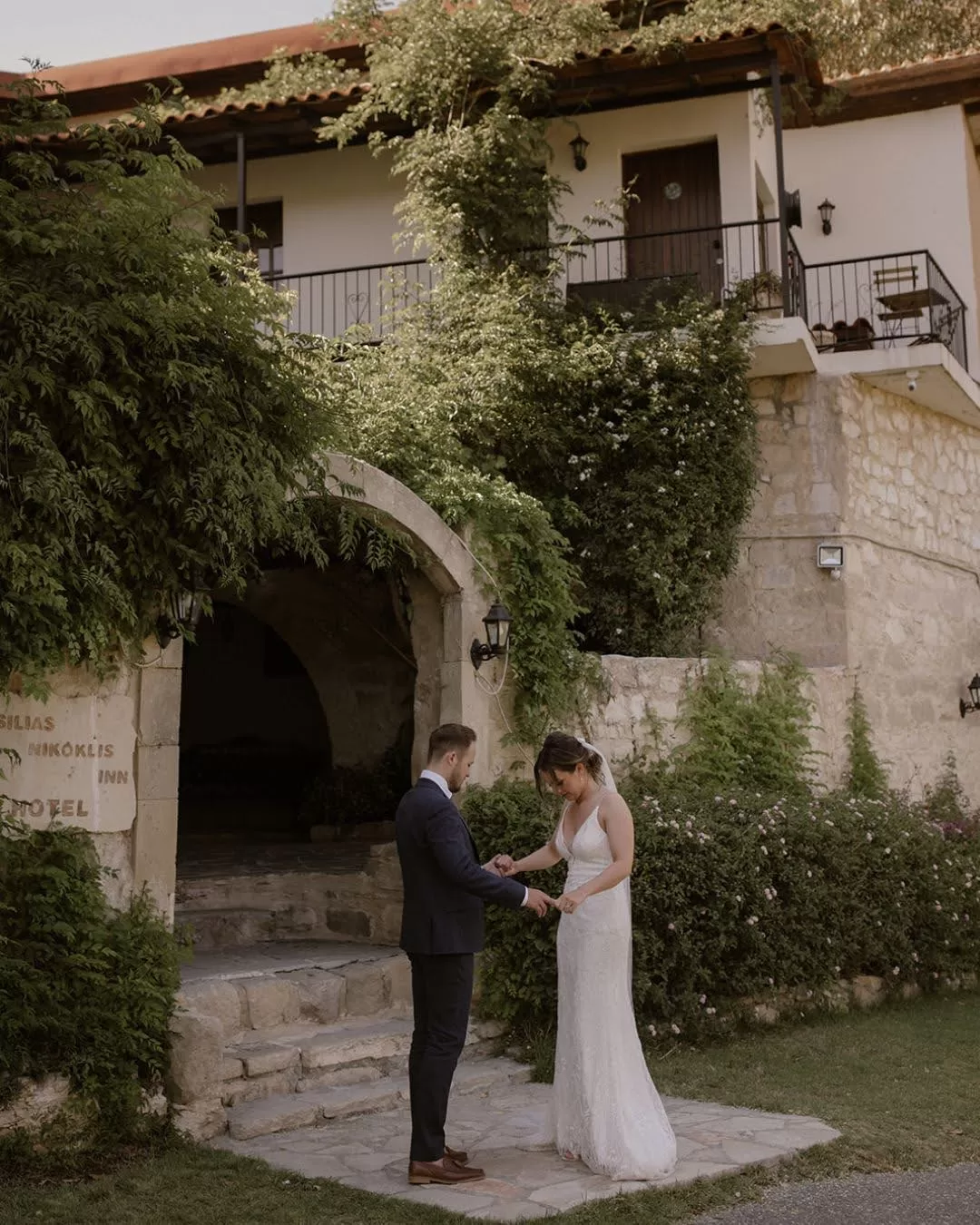 Bride and groom under the stone archway of Vasilias Nikoklis Inn, framed by olive trees and warm Mediterranean light.