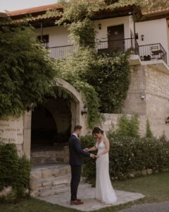 Bride and groom under the stone archway of Vasilias Nikoklis Inn, framed by olive trees and warm Mediterranean light.