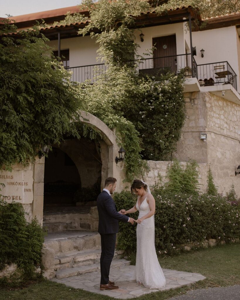 Bride and groom under the stone archway of Vasilias Nikoklis Inn, framed by olive trees and warm Mediterranean light.