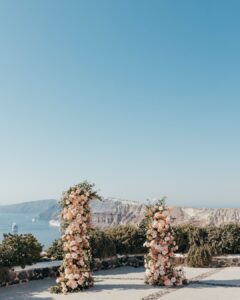 Stunning floral arch with white roses and greenery set against the whitewashed walls of Venetsanos Winery, captured by Sarah Elizabeth.