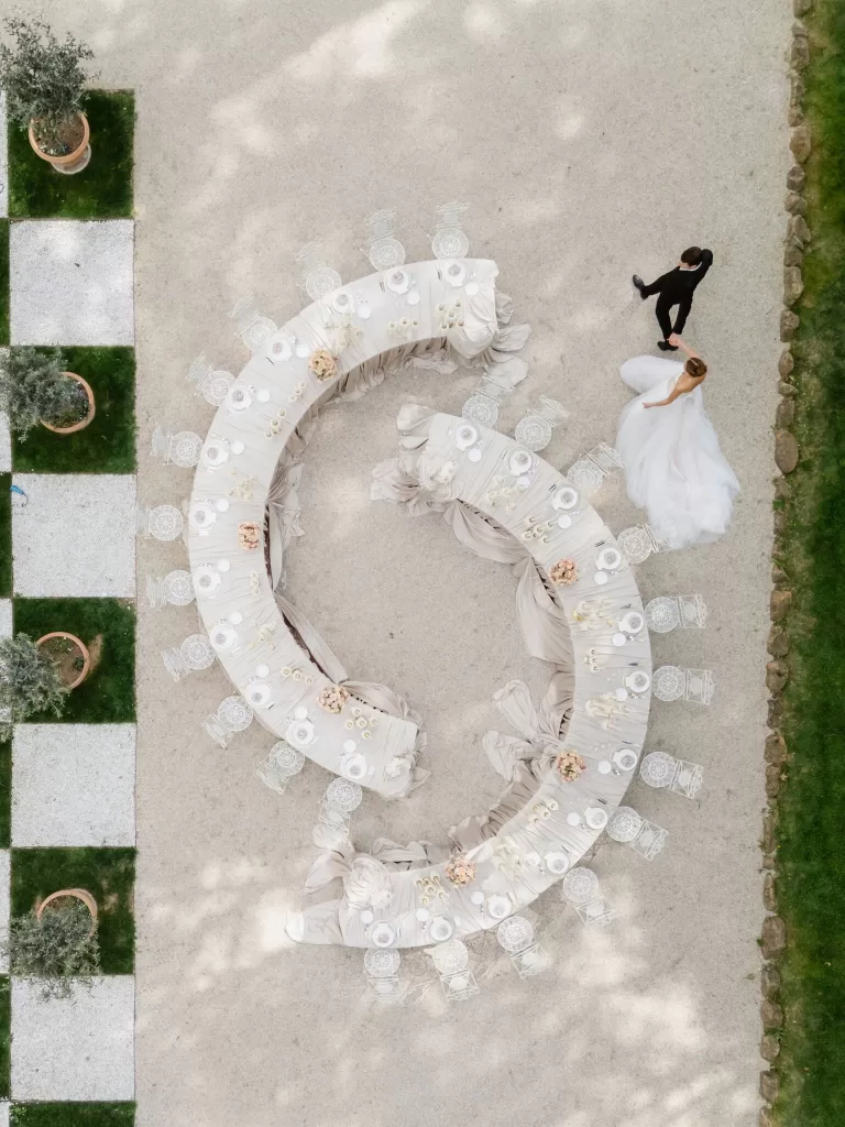 Bride and groom walking beside elegant S-shaped table setup in Villa Aurelia courtyard