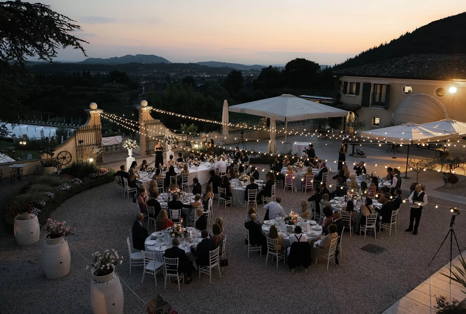 Guests enjoying a romantic outdoor wedding dinner at Villa Cariolla under string lights as the sun sets over the hills.