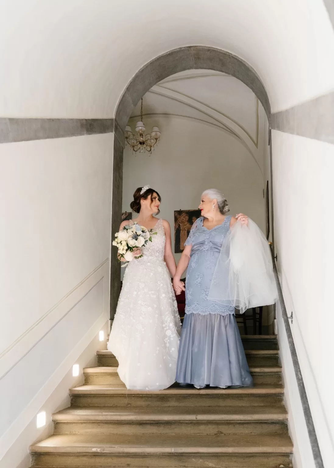 Bride and her mother smiling warmly at each other as they descend the staircase at Villa Ivana.