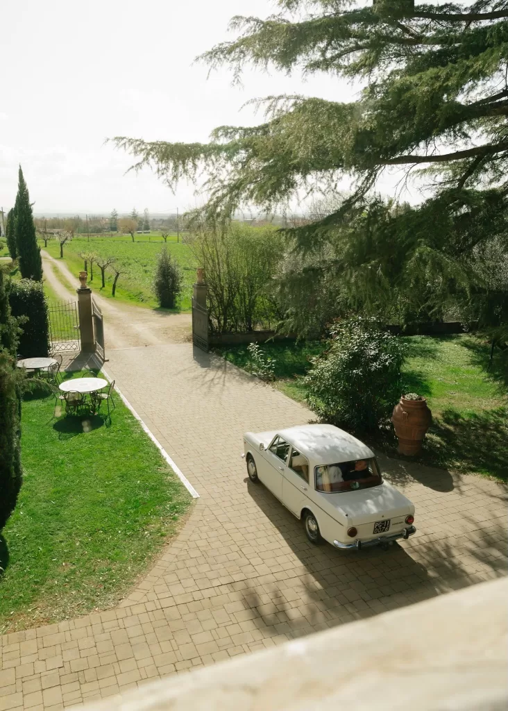 Vintage white wedding car driving through the countryside driveway of Villa Ivana.