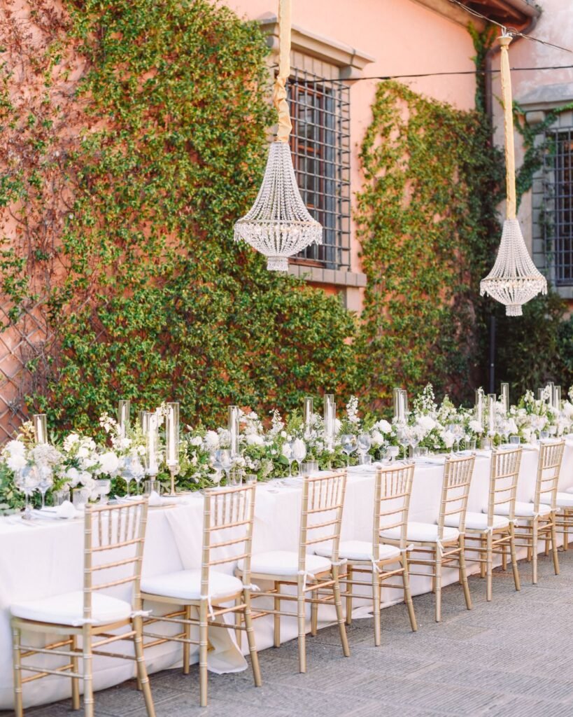 Detailed view of chic dining decor at Villa Mangiacane wedding, highlighting crystal chandeliers, delicate florals, and gold seating.