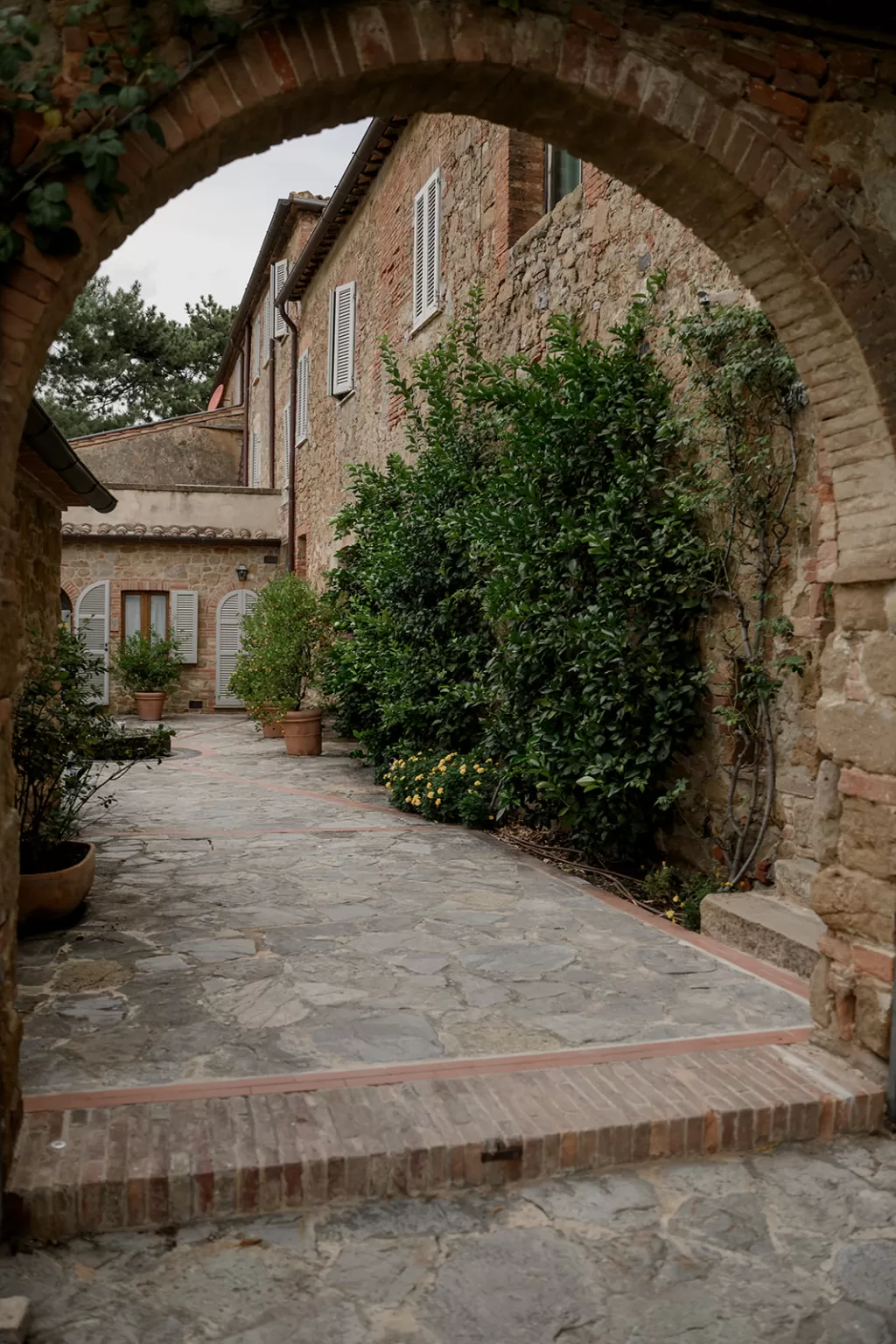 Stone archway framing a peaceful courtyard at Borgo Sant Ambrogio, with rustic walls and greenery creating a romantic Italian charm