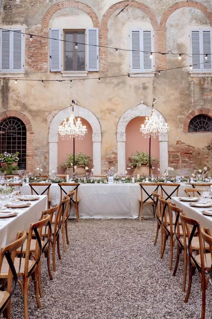 Long reception tables in the courtyard of Borgo Sant'Ambrogio with hanging chandeliers and soft lighting.