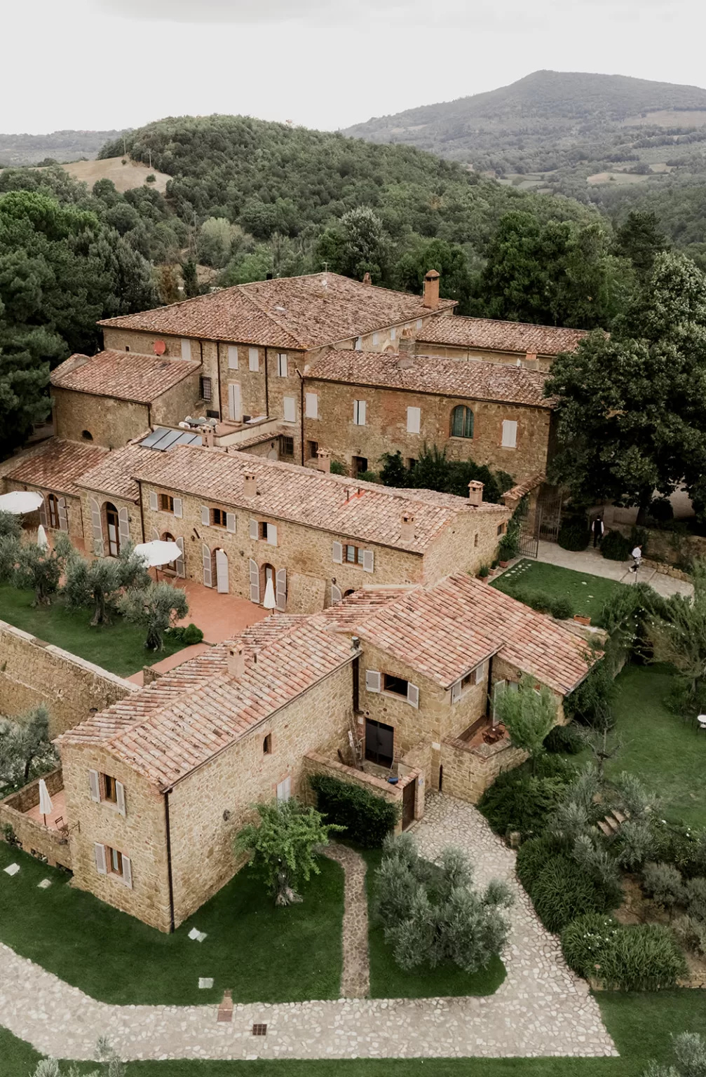 Aerial view of Borgo Sant’Ambrogio’s villa and olive-lined paths, surrounded by Tuscan hills and forest.